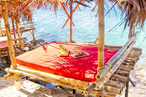 A bamboo-framed beach chair with a red cushion and a plate of food, overlooking the sea.