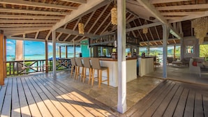 A wooden deck with a bar area, outdoor seating, and a view of the ocean.