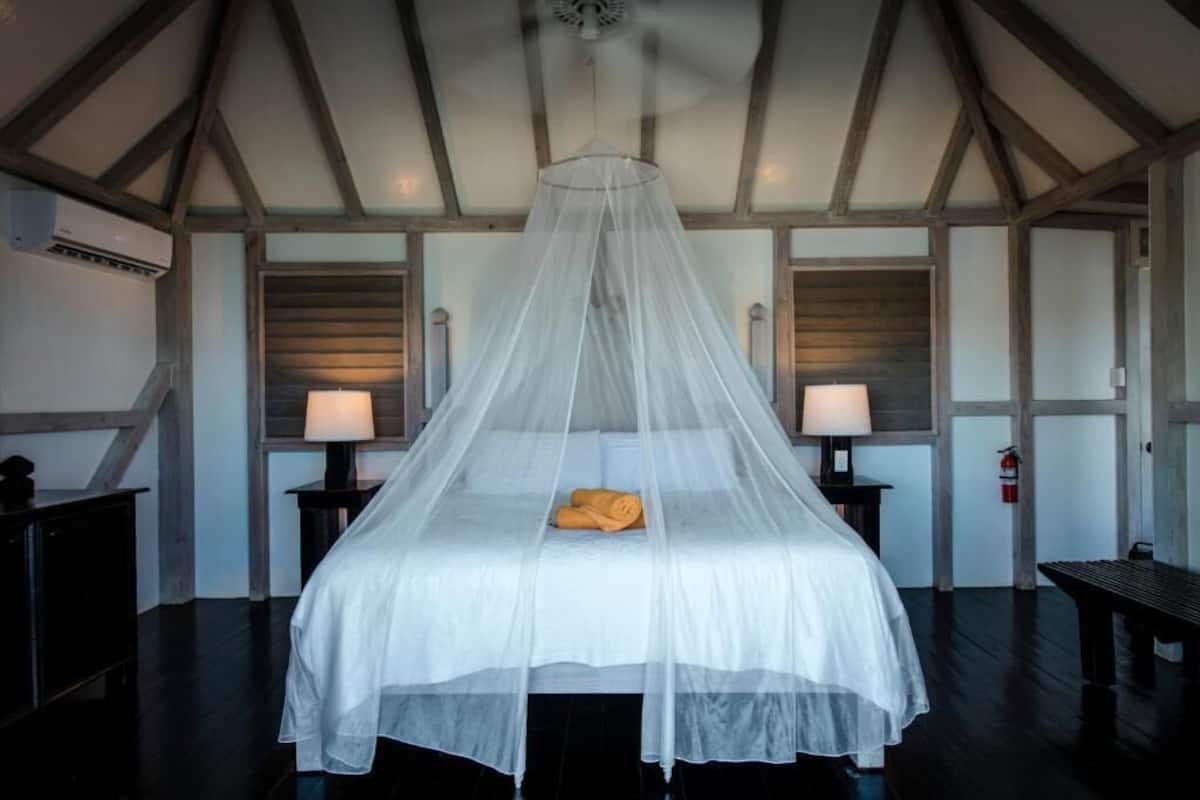 A room with a bed under a canopy, two bedside tables with lamps, and a fire extinguisher on the wall.