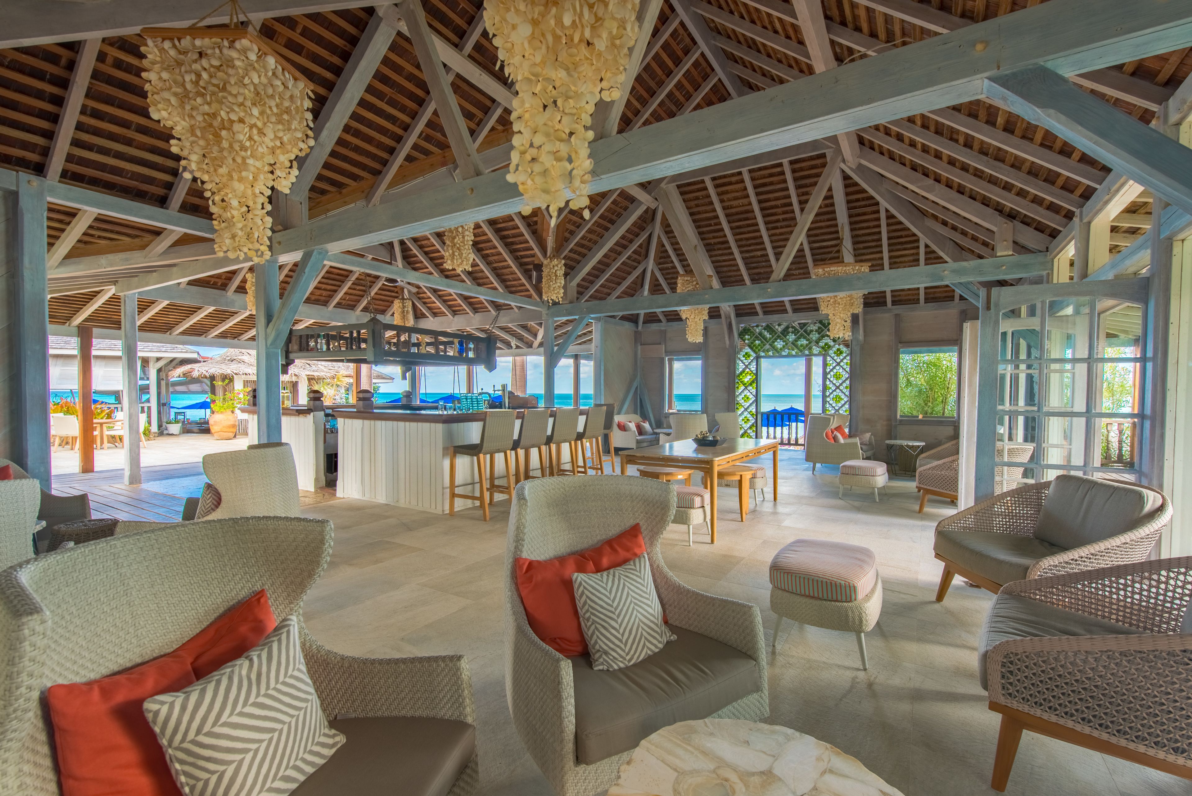A spacious indoor area with wicker furniture, a bar, and large windows offering views of the ocean.