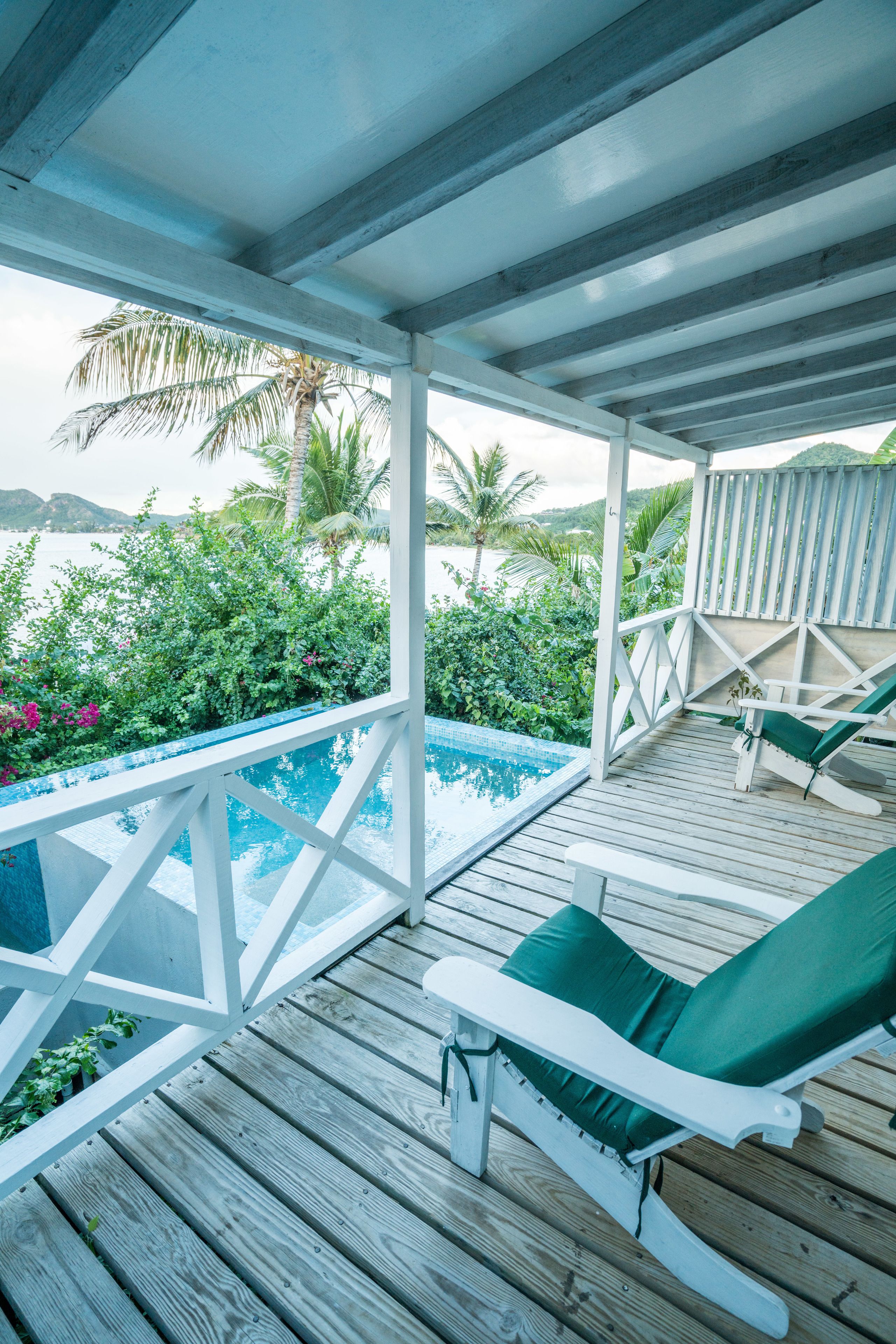 A wooden deck with a pool, lounge chairs, and a view of the sea and greenery.