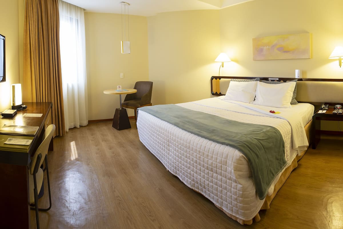 A hotel room with a bed, bedside tables, a desk, a chair, a TV, and a lamp.
