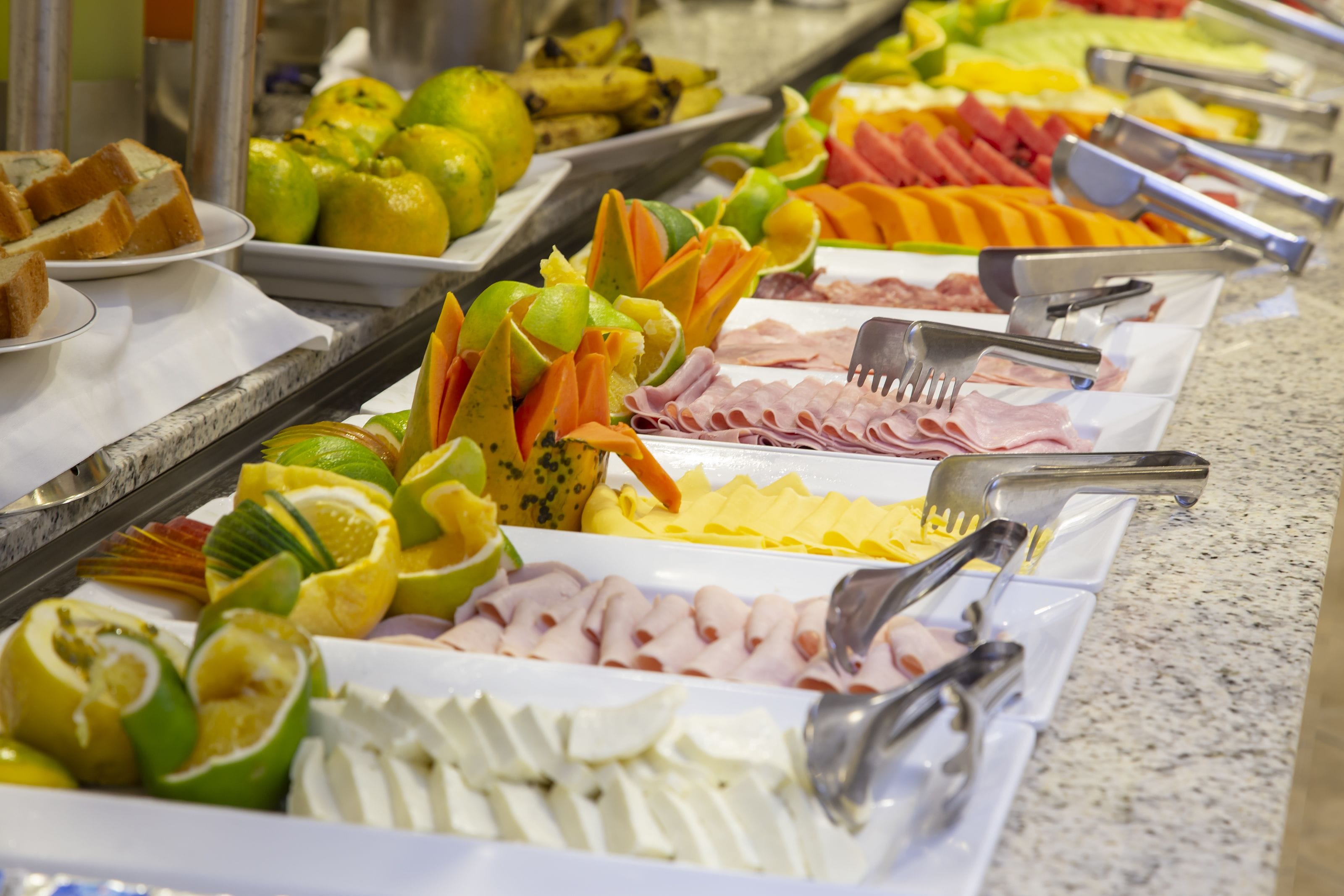 A buffet with various food items including sliced meats, cheeses, and fruits.