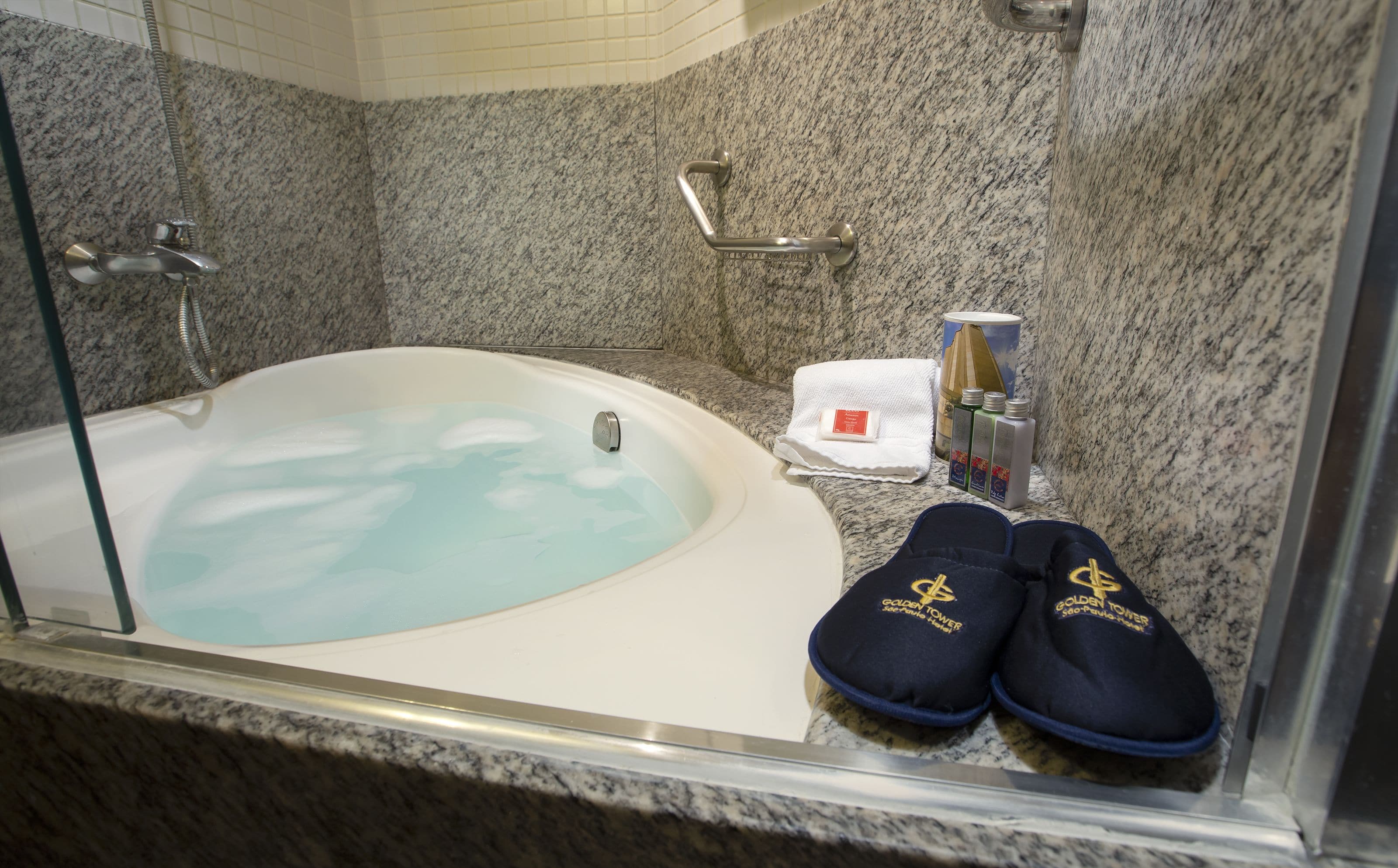 A bathroom with a bathtub, a shower, and a glass-enclosed shower area. There are slippers, a towel, and toiletries on the counter.