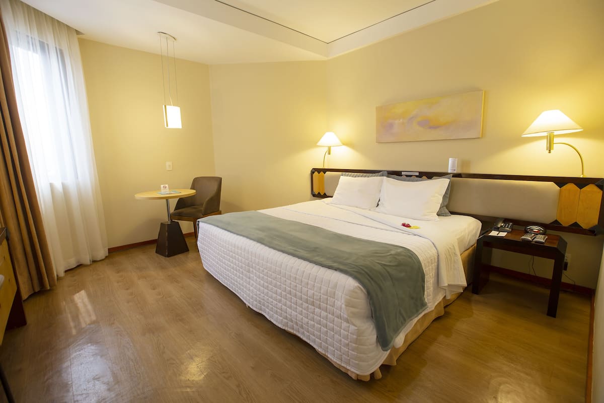 A hotel room with a large bed, two bedside lamps, a small table, and a chair.