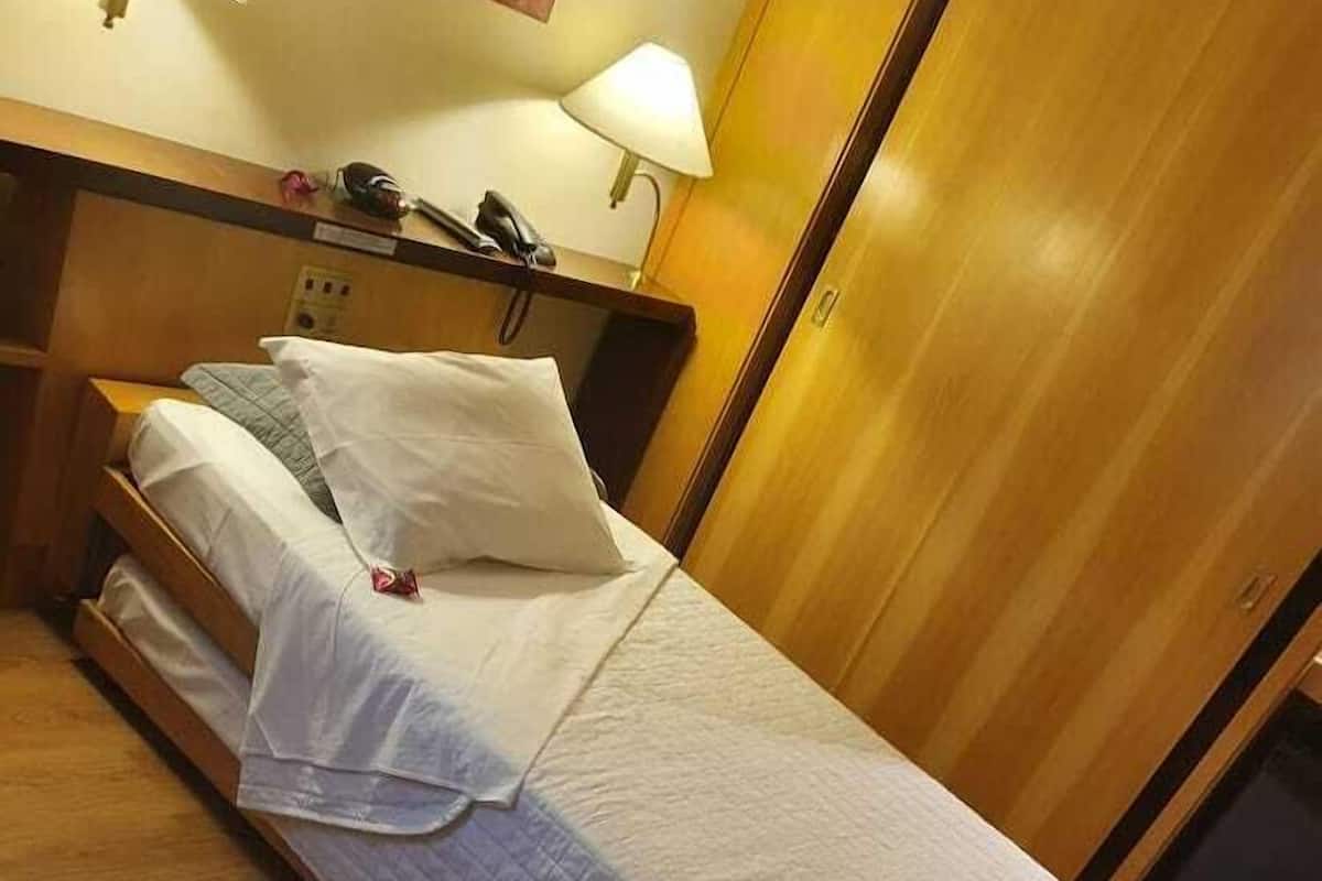A single bed with white linens in a room with wooden flooring and a wooden headboard.