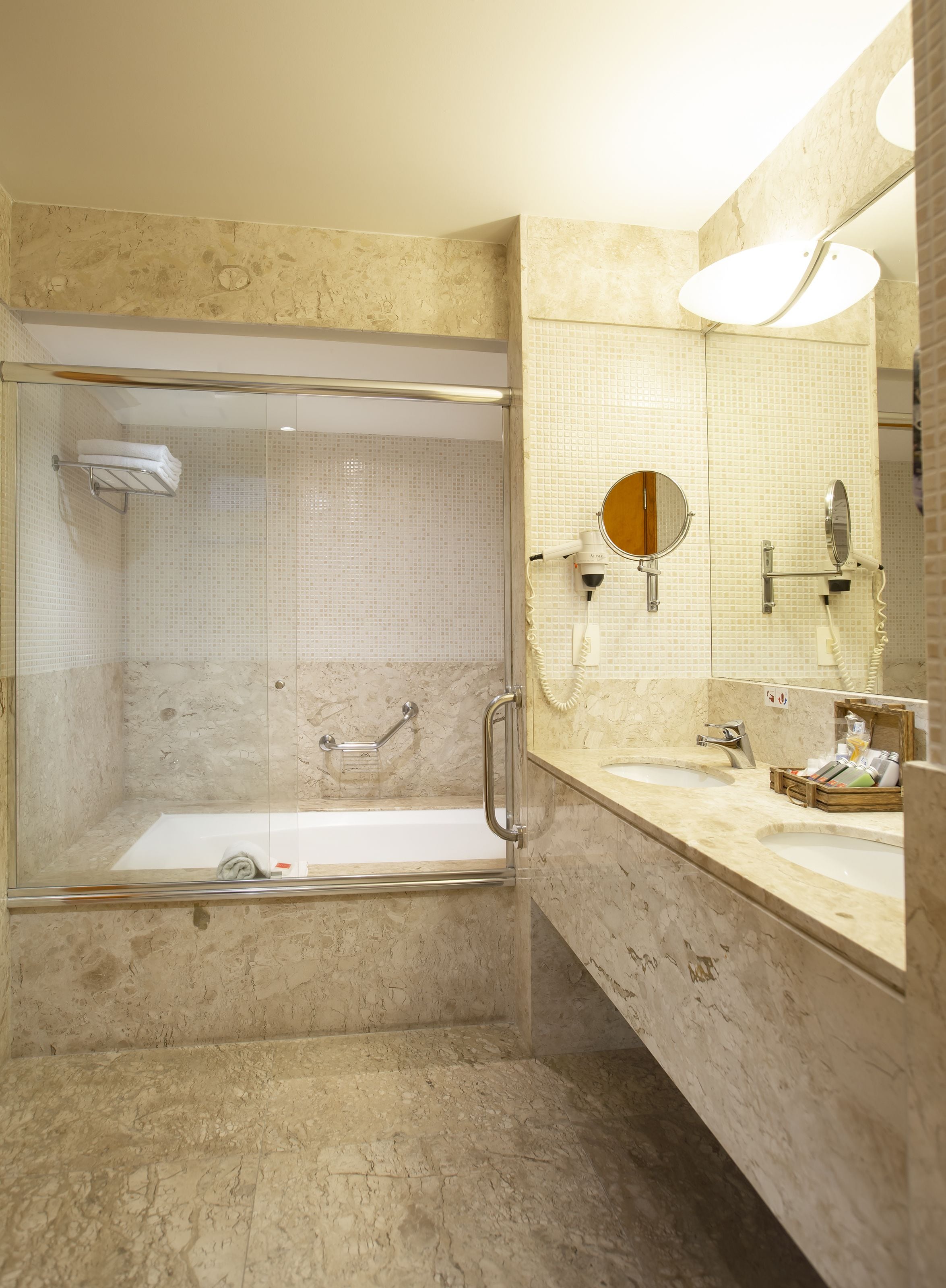 Une salle de bain moderne dotée d’une douche à parois de verre, d’un meuble-lavabo avec un grand miroir et d’un mur recouvert de carreaux de marbre.