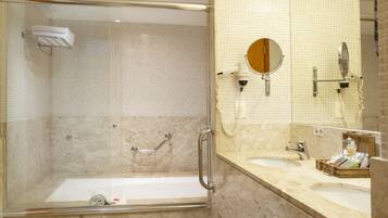 Un baño moderno con ducha de vidrio, tocador con espejo grande y pared revestida de mármol.