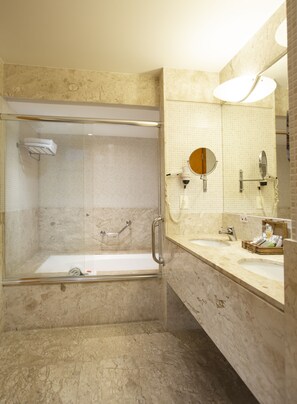 A modern bathroom with a glass-enclosed shower, a vanity with a large mirror, and a marble-tiled wall. - Golden Tower Pinheiros by Fênix Hotéis (São Paulo)