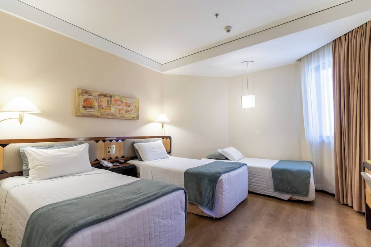 A hotel room with two beds, a painting on the wall, and a window with curtains.