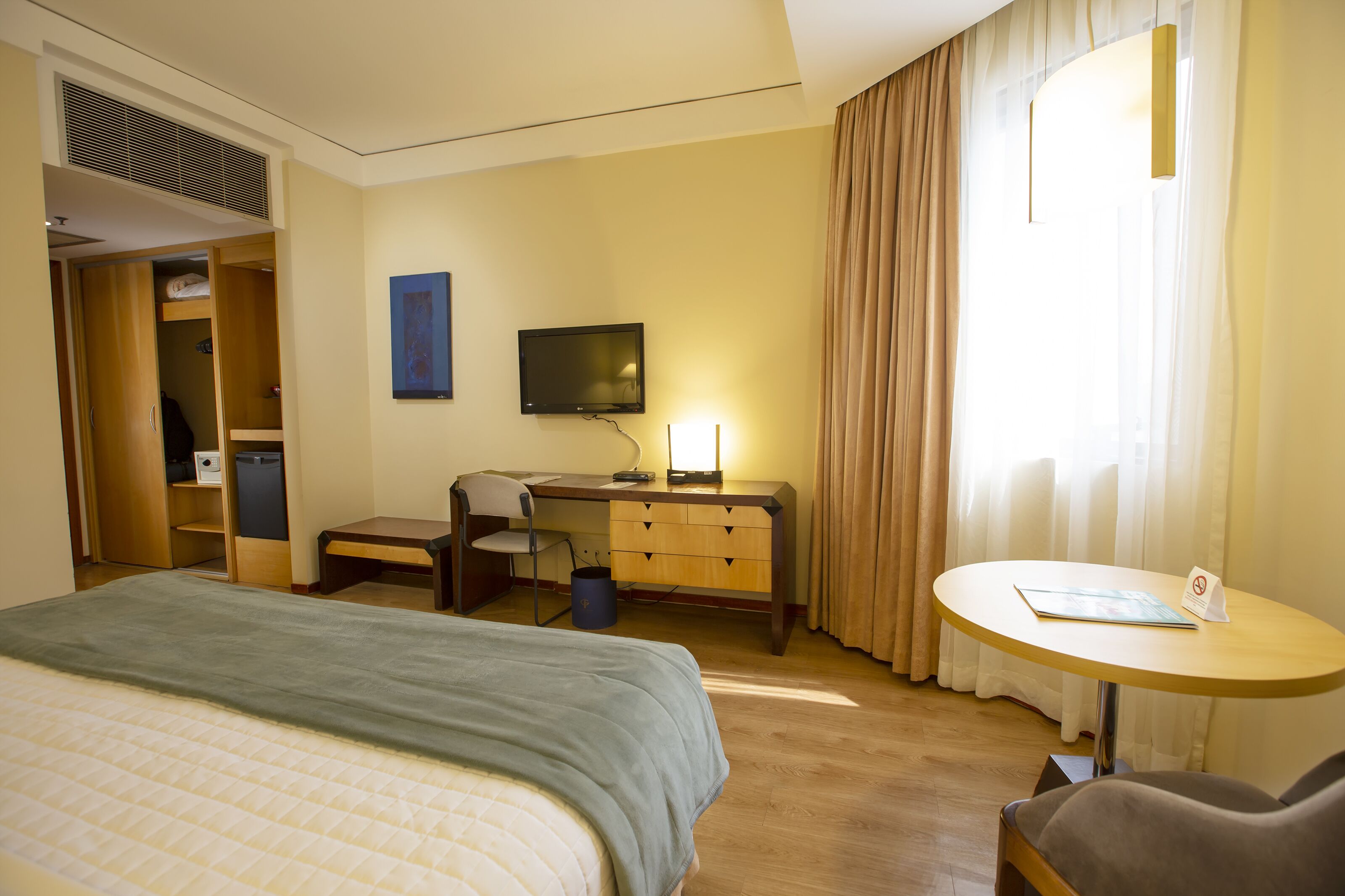 A hotel room with a bed, desk, chair, and a small table with a sign.
