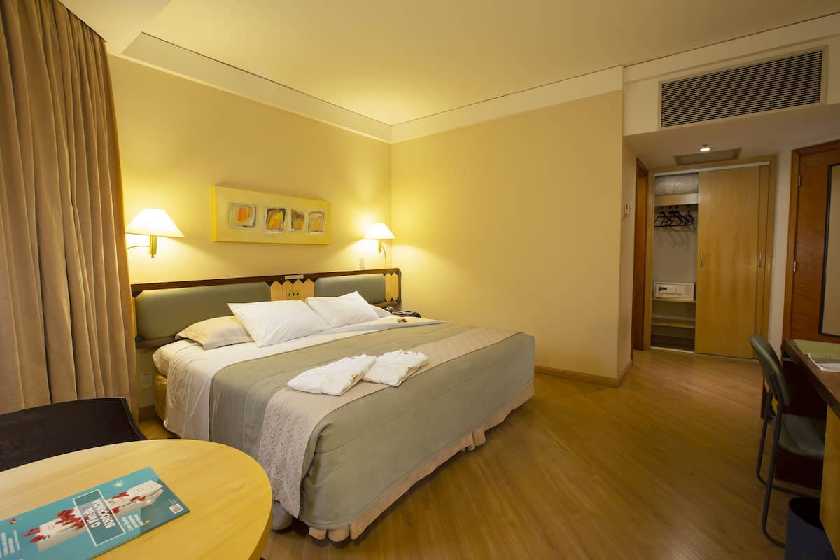 A hotel room with a bed, two bedside lamps, a desk, and a chair.