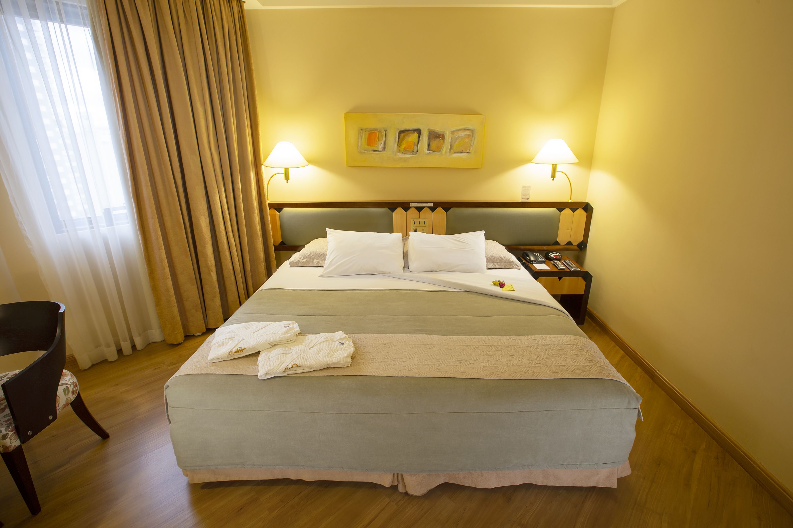 Habitación de hotel con cama, dos lámparas de noche, un cuadro en la pared y una silla.