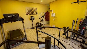 Un gimnasio con cinta de correr, elíptica y varios pesas.
