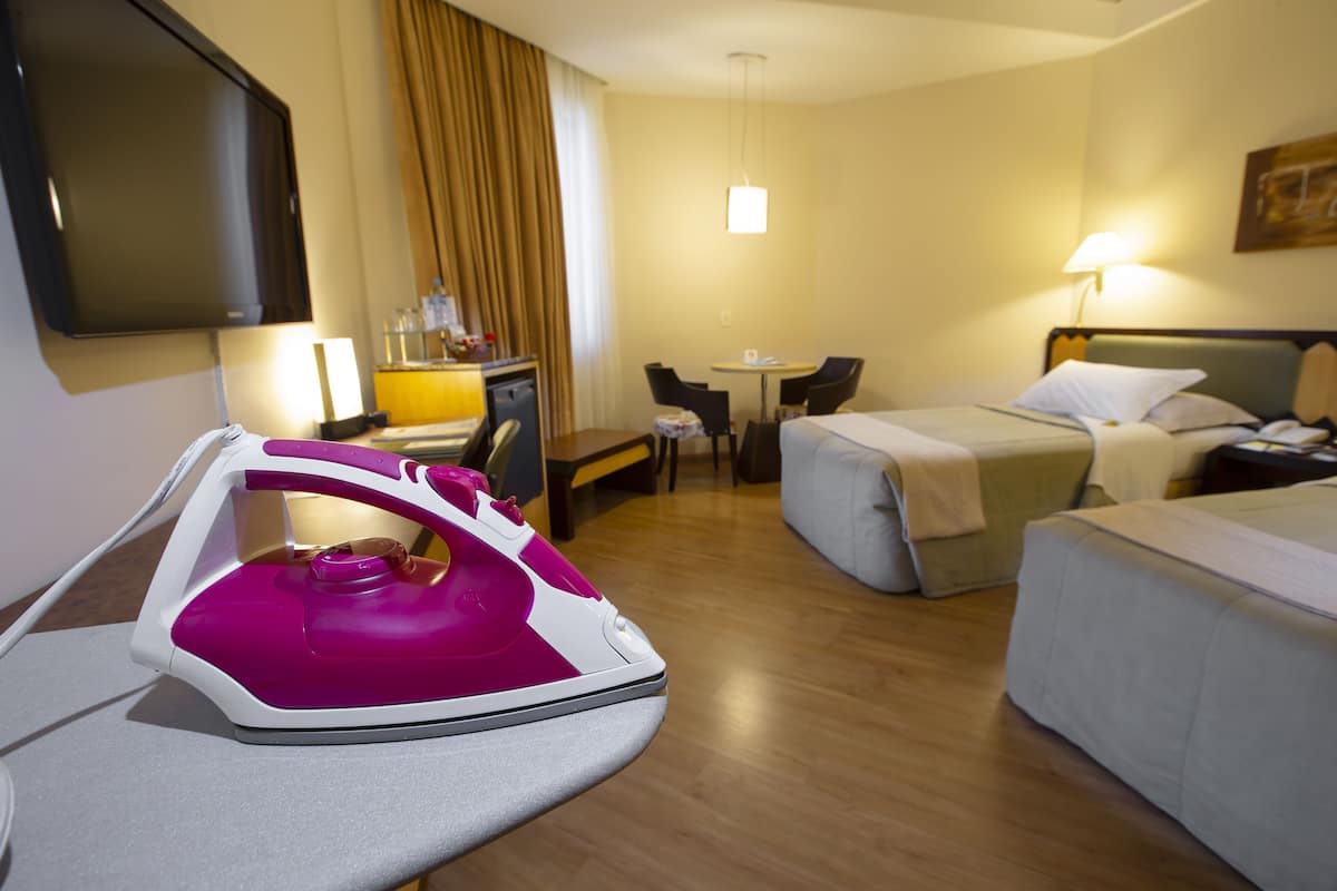 A hotel room with two beds, a desk, a chair, a TV, and an iron.