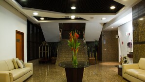 A lobby with a glass-top table, two sofas, a staircase, and a reception desk. - Golden Tower Pinheiros by Fênix Hotéis (São Paulo)