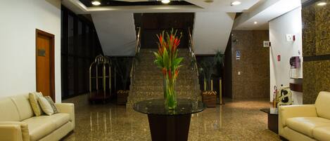A lobby with a glass-top table, two sofas, a staircase, and a reception desk.