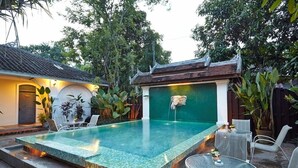 Una piscina con borde de azulejos, rodeada de mobiliario de exterior y plantas.