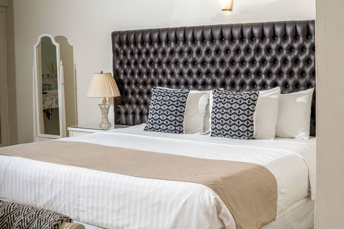 Una cama bien hecha con cabecera capitonada, una lámpara de noche y almohadas estampadas.