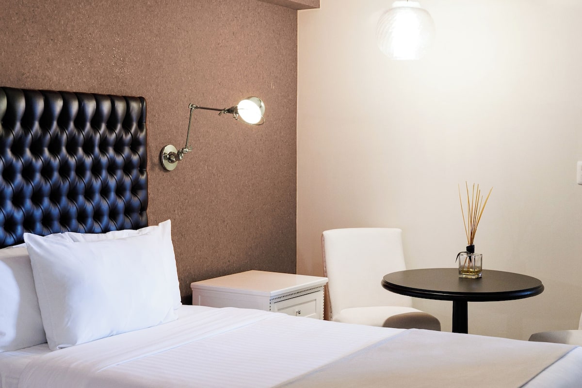 Habitación de hotel con una cama grande, una mesita de noche, una silla y una pequeña mesa con lámpara.