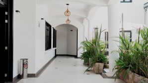 A clean, white hallway with a modern light fixture, potted plants, and a trash bin. - Casa Bonita Hotel & Luxury Residence (Oaxaca)