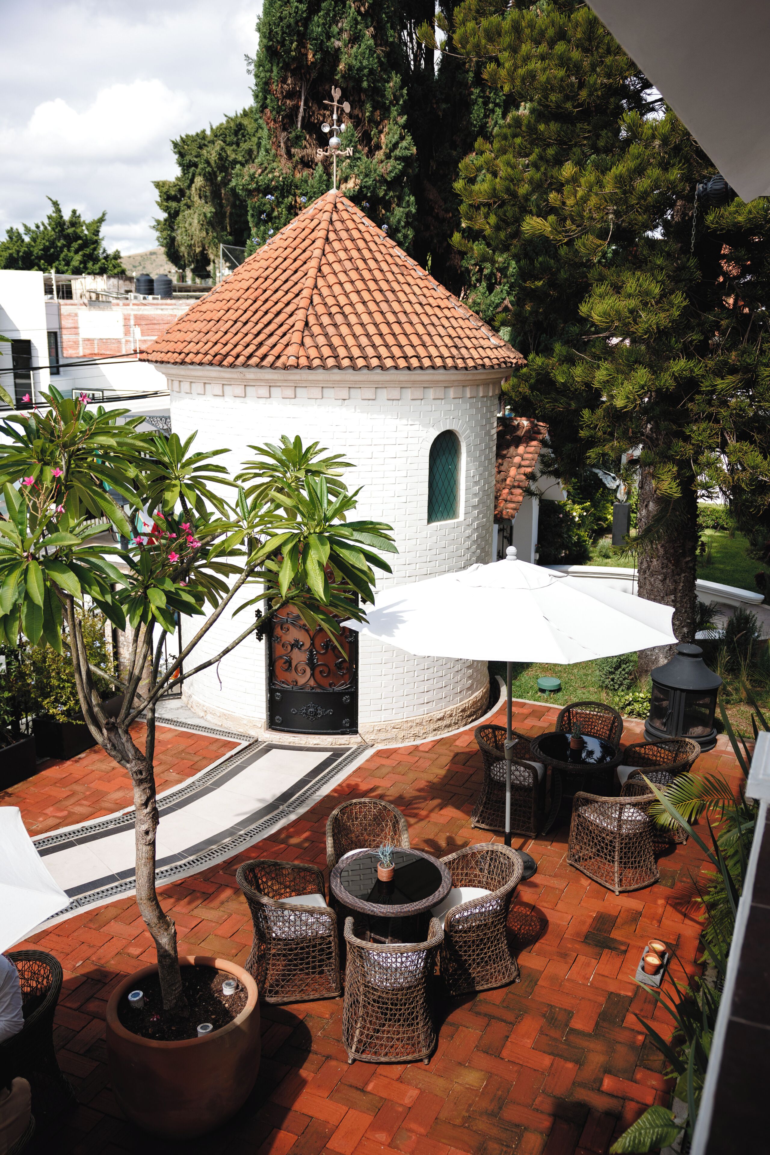 A courtyard with a small white building, wicker furniture, and potted plants.