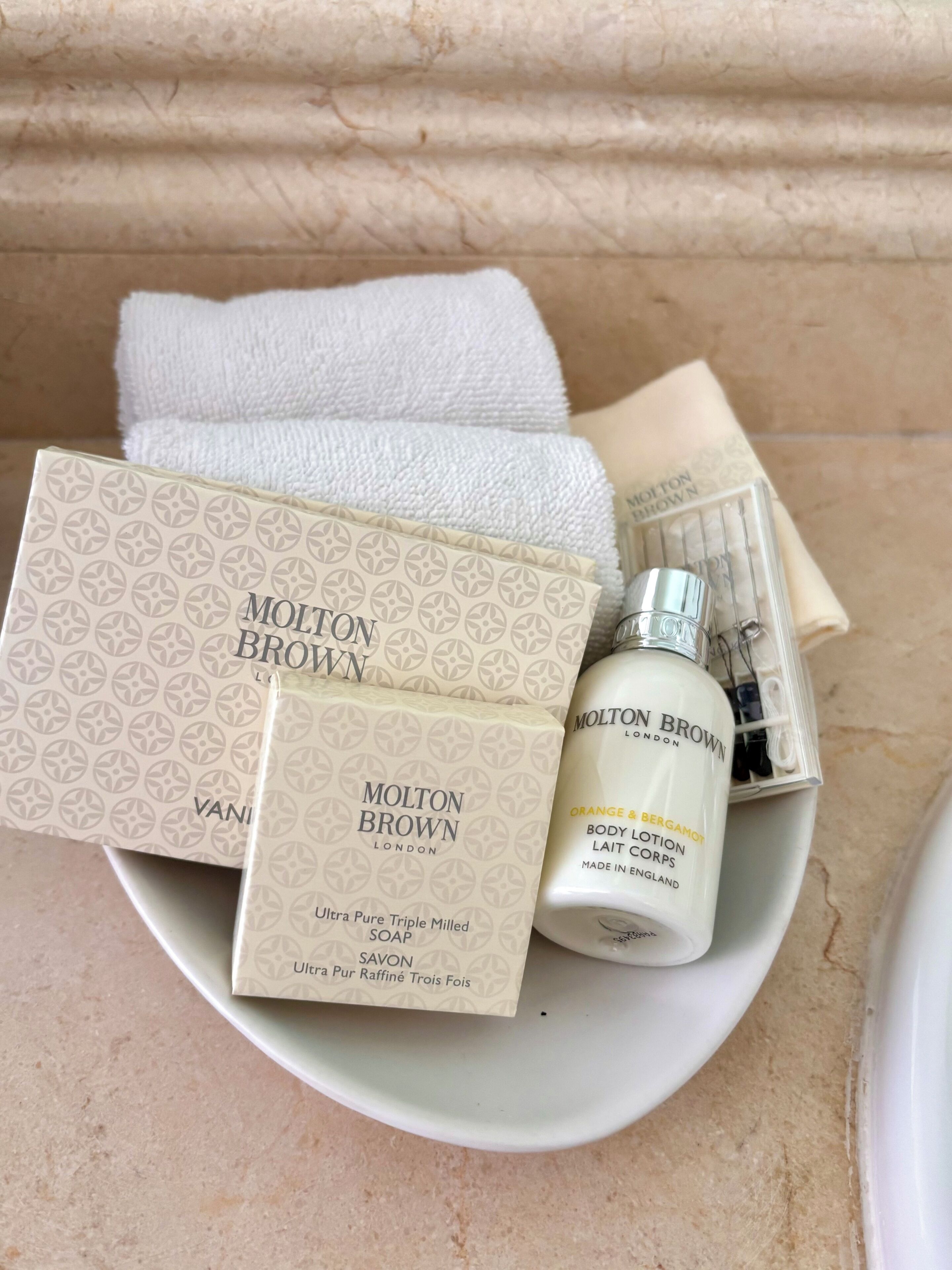 A collection of toiletries including a bottle of lotion and several boxes of soap, arranged on a white plate.