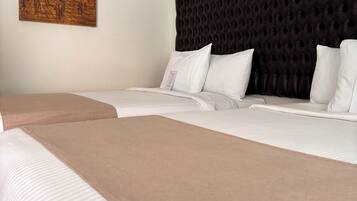 Quarto de hotel com duas camas, cabeceira escura, roupa de cama branca e luminária fixada na parede.