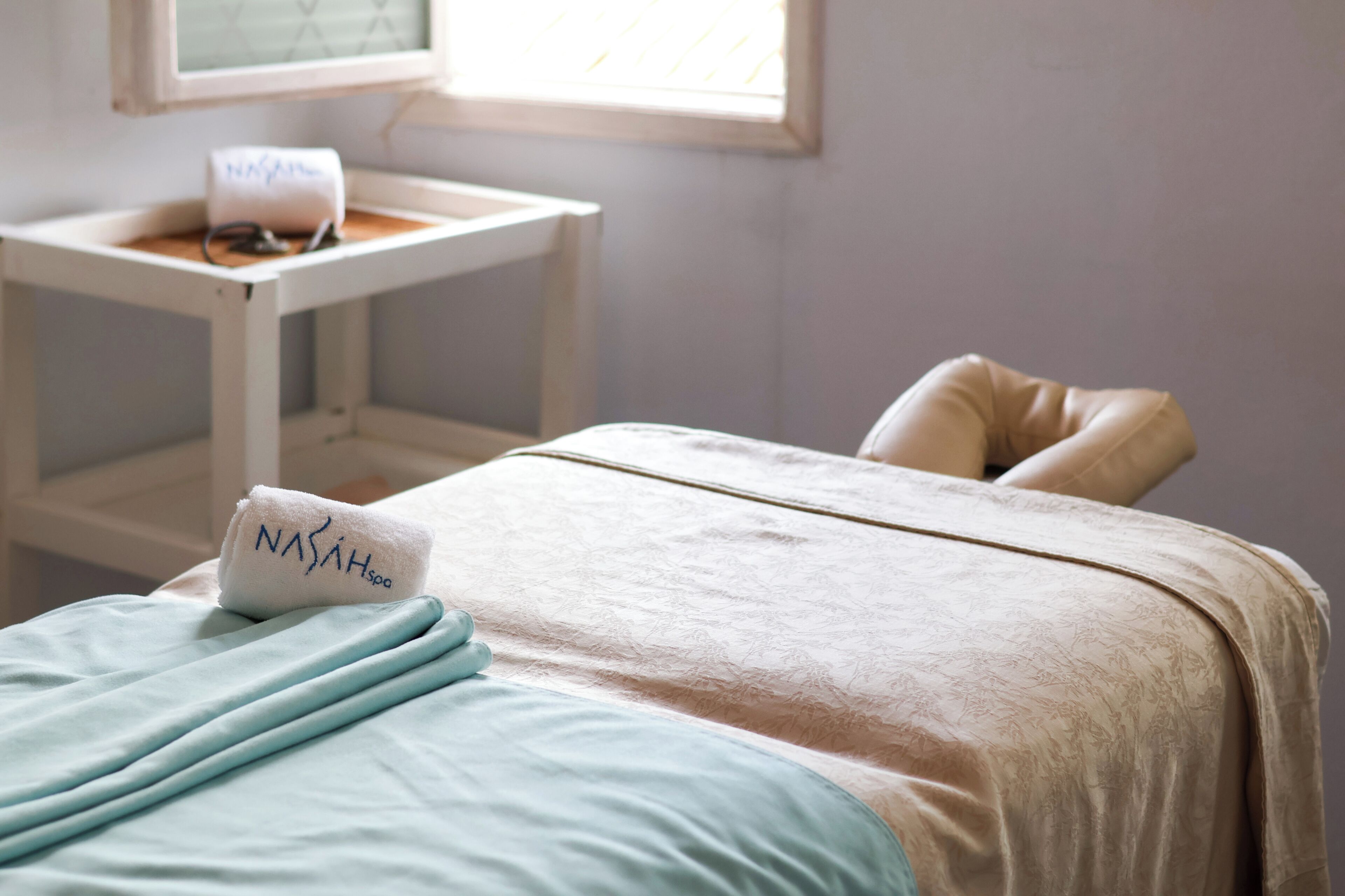 Une chambre d’hôtel avec un lit, un fauteuil massant, une petite table avec une lampe et une fenêtre.