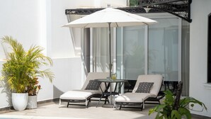 Een zwembadgedeelte met ligbedden, een tafel en een grote parasol.