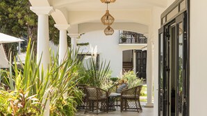 A covered outdoor area with a tiled floor, wicker furniture, and potted plants. - Casa Bonita Hotel & Luxury Residence (Oaxaca)