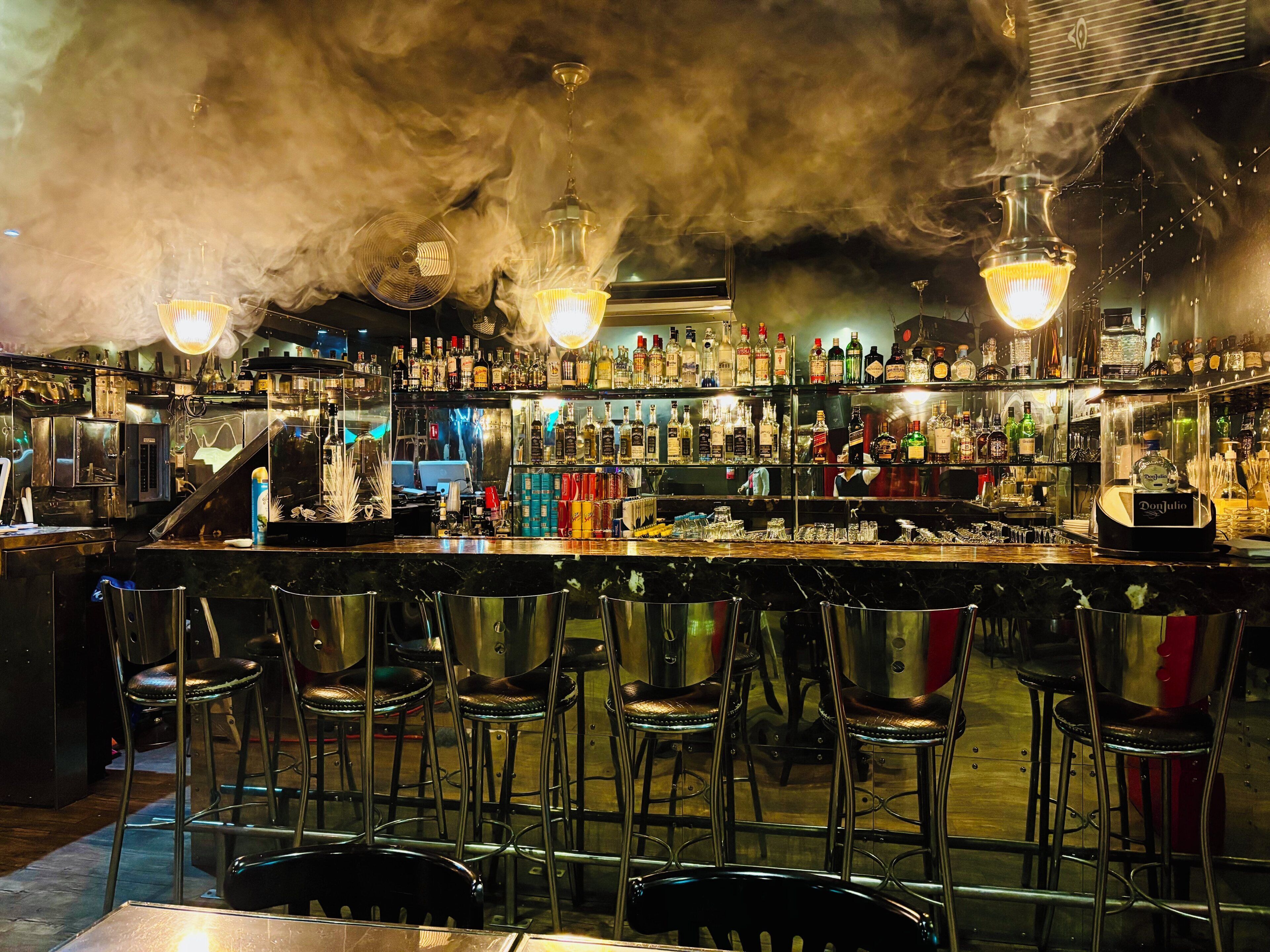 A bar with multiple stools, a variety of bottles, and a bar counter.