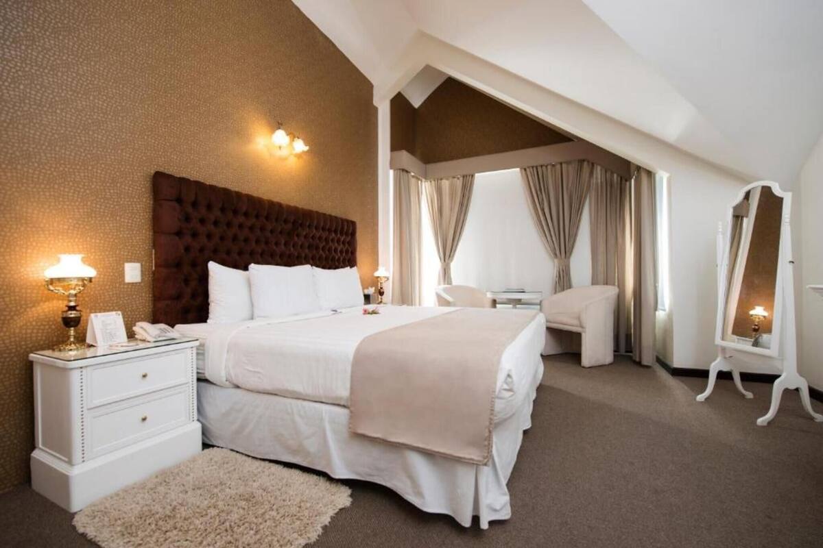 A bedroom with a large bed, bedside tables, a chair, a mirror, and a window with curtains.