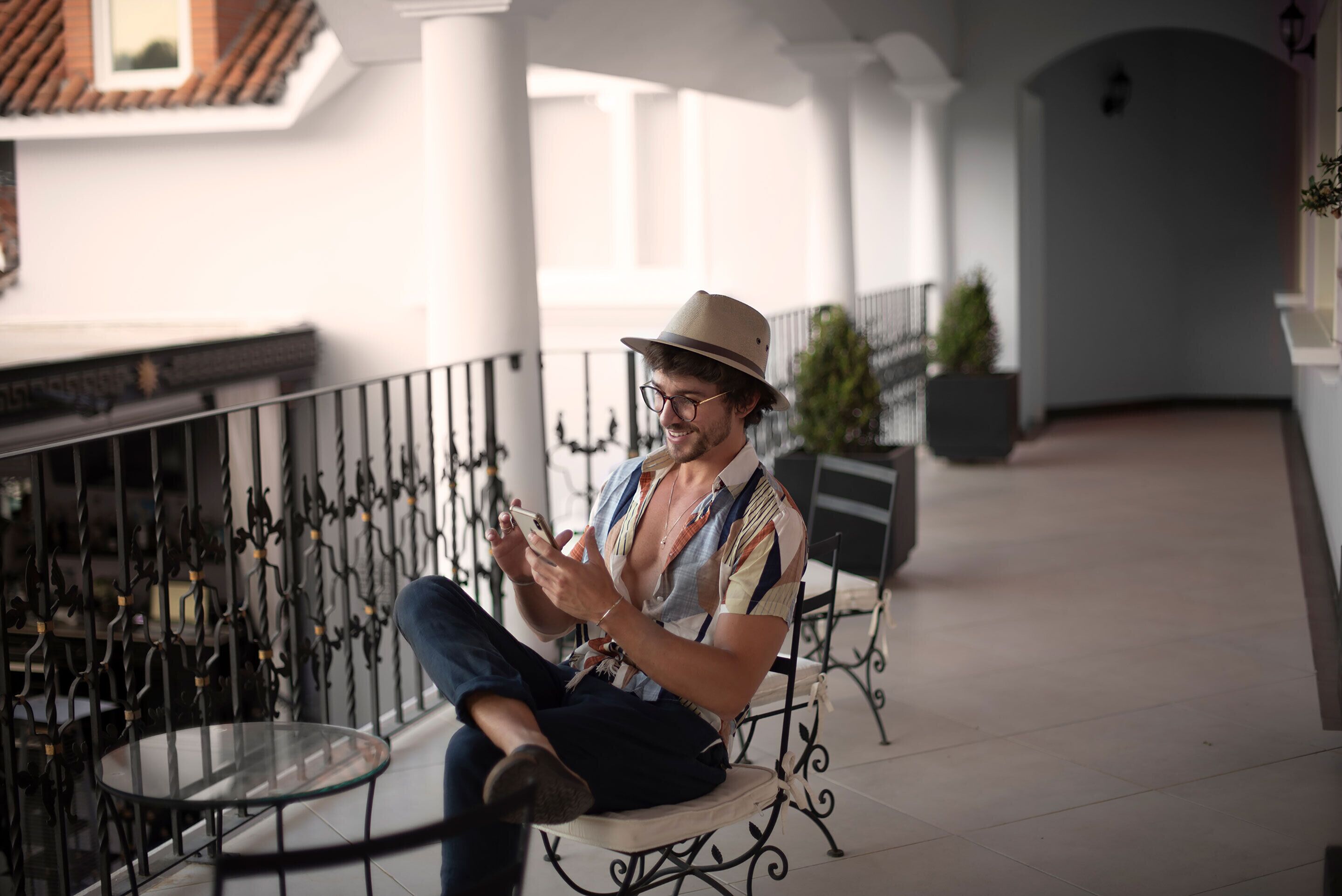 A man sitting on a bench in a covered outdoor area with metal railings and a glass table.