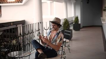 A man sitting on a bench in a covered outdoor area with metal railings and a glass table.