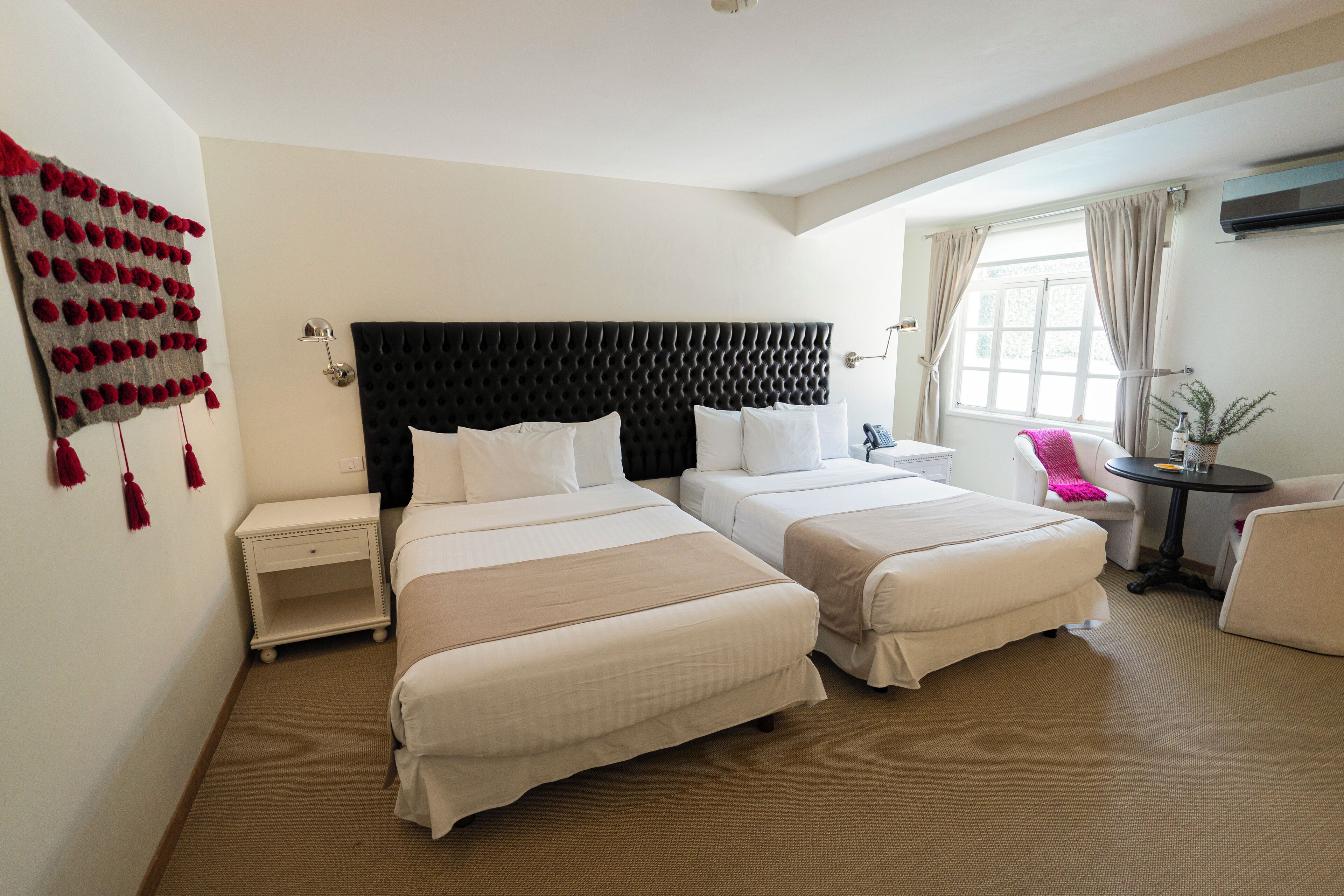 A hotel room with two beds, a nightstand, a small table, and a chair.