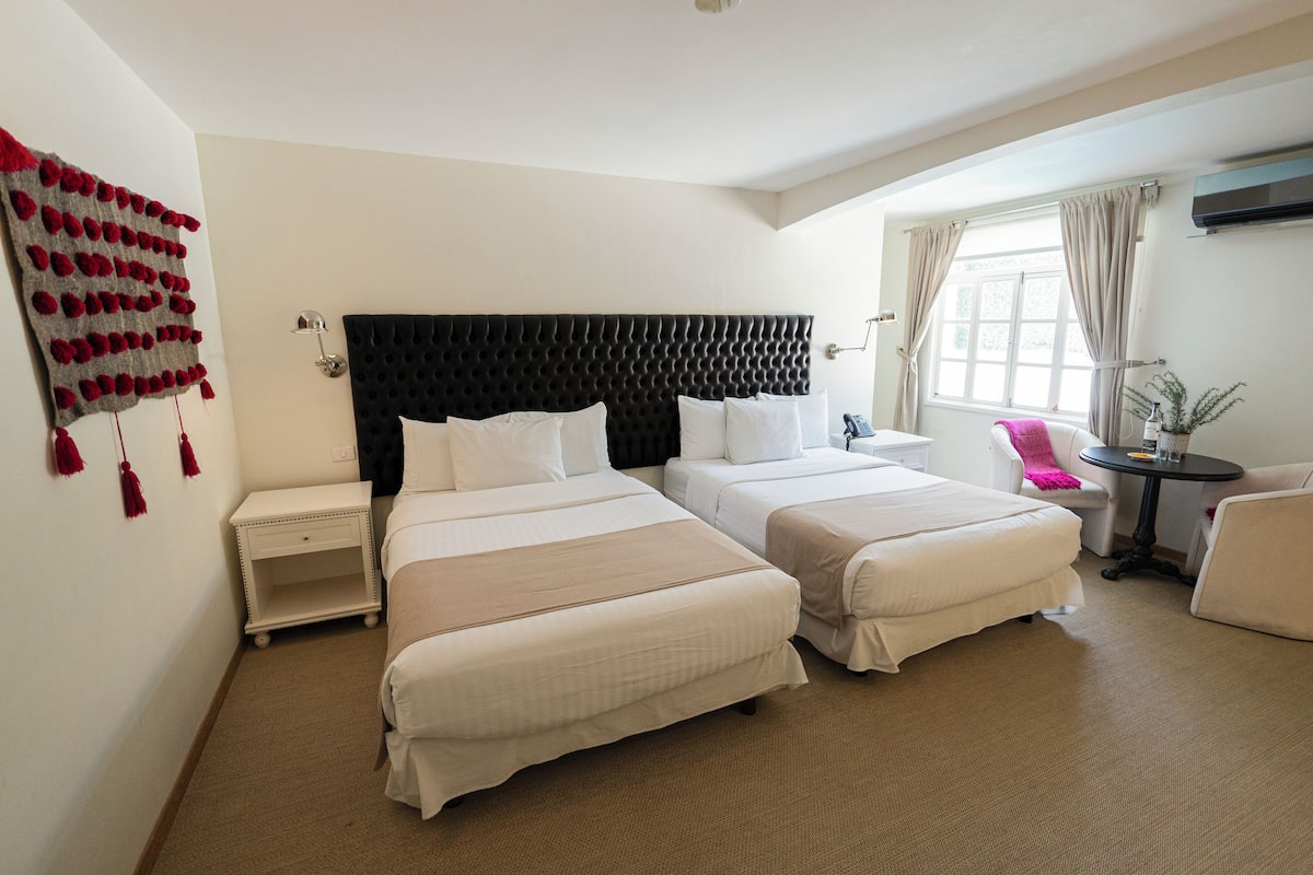 A hotel room with two beds, a nightstand, a small table, and a chair.