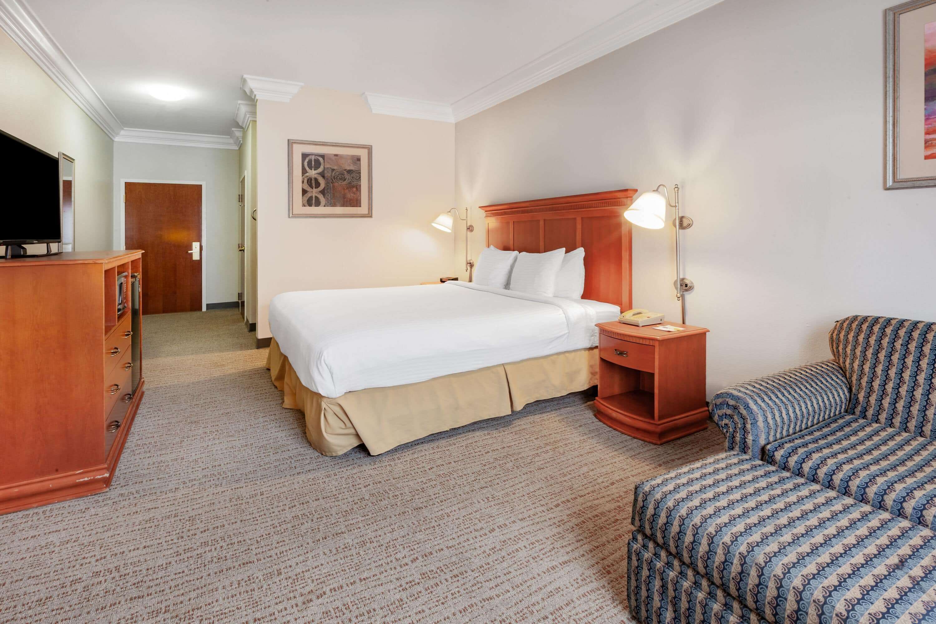 Ein Hotelzimmer mit einem großen Bett, Nachttischen, einem Fernseher, einem Schreibtisch und einem gemusterten Sessel.