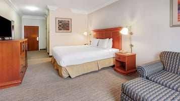 Ein Hotelzimmer mit einem großen Bett, Nachttischen, einem Fernseher, einem Schreibtisch und einem gemusterten Sessel.