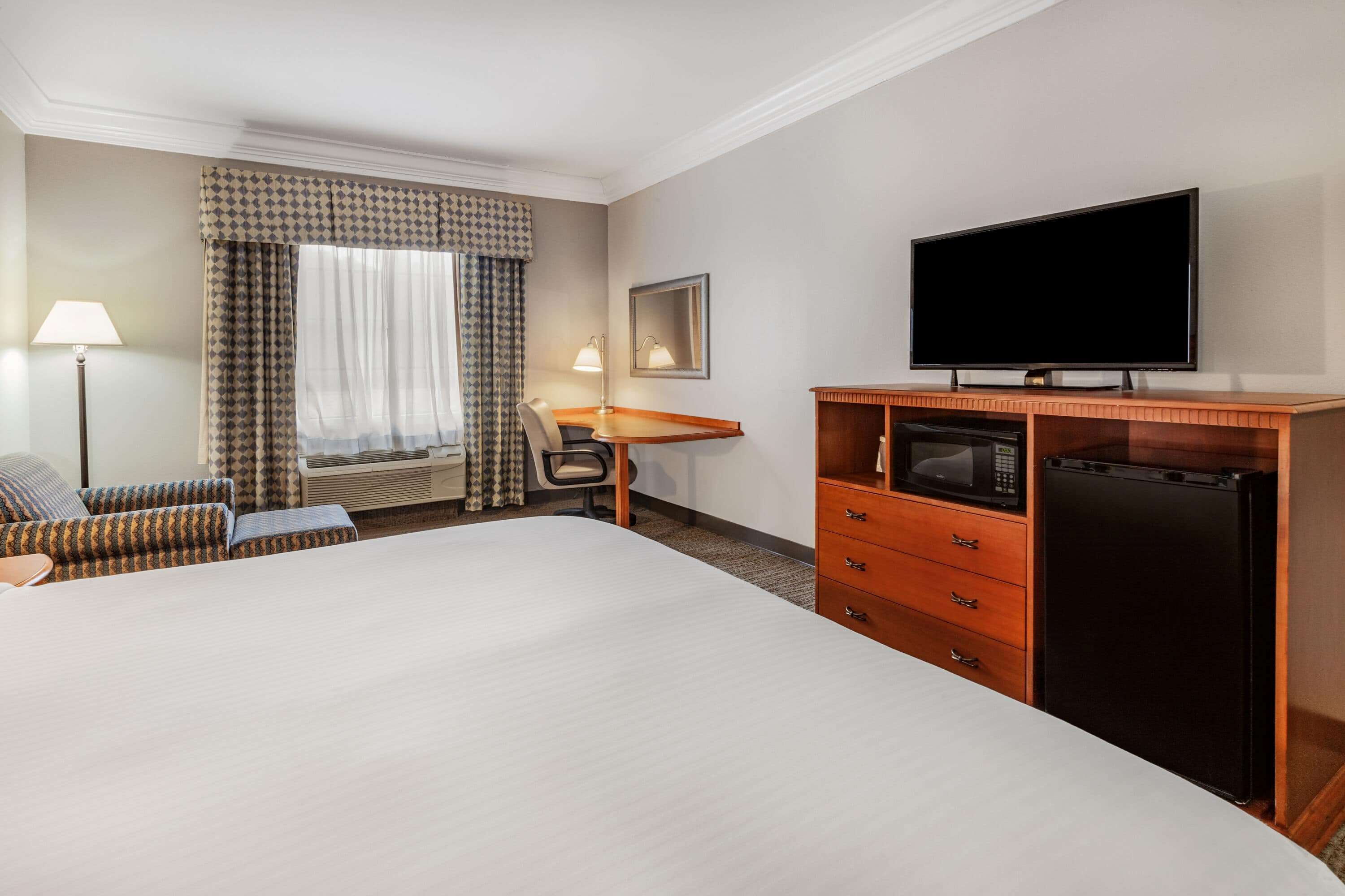 Habitación de hotel con una cama grande, un escritorio con silla, televisor, microondas y refrigerador.