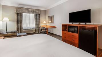Habitación de hotel con una cama grande, un escritorio con silla, televisor, microondas y refrigerador.