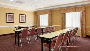 A conference room with a long table, red chairs, and two framed pictures on the wall.