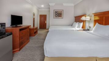 A hotel room with two beds, a television, a desk with drawers, a lamp, and a painting on the wall.