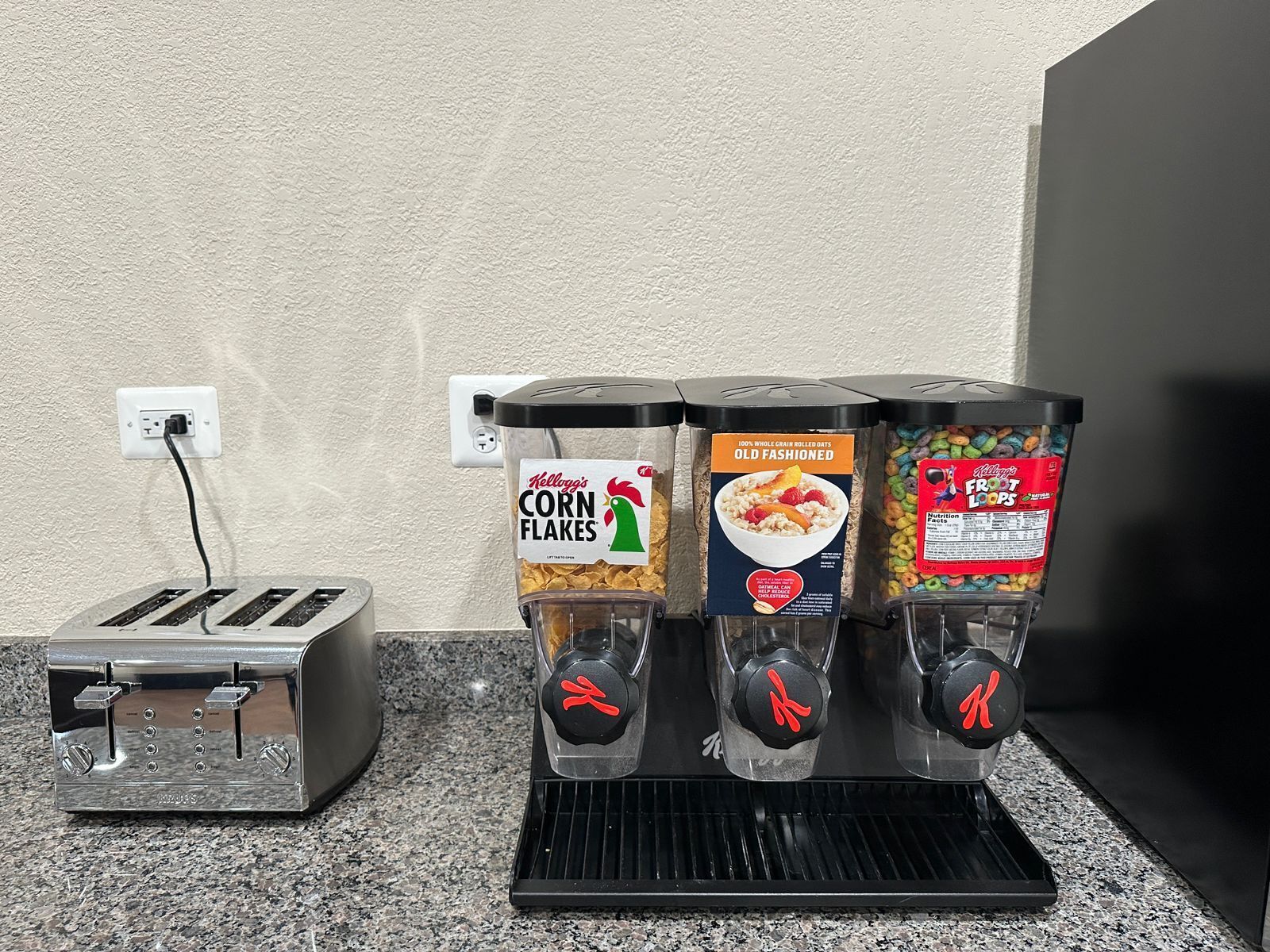 A kitchen with a toaster, three beverage dispensers, and a wall socket.