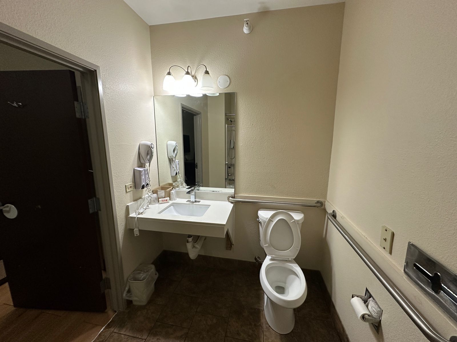 A bathroom with a sink, mirror, toilet, and hand dryer.
