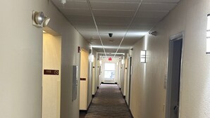 A long, narrow hallway with carpeted floors, doors on both sides, and a ceiling with recessed lighting and a smoke detector.