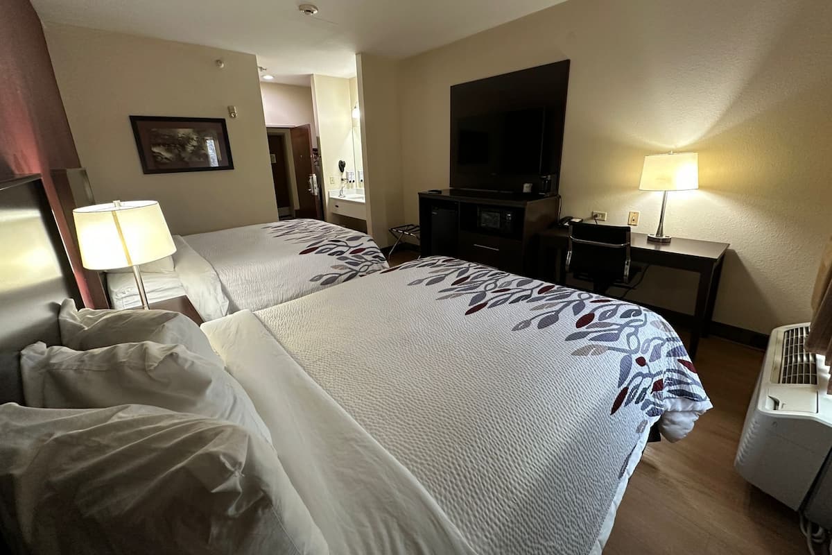 A hotel room with two beds, a TV, a desk, and a heater.