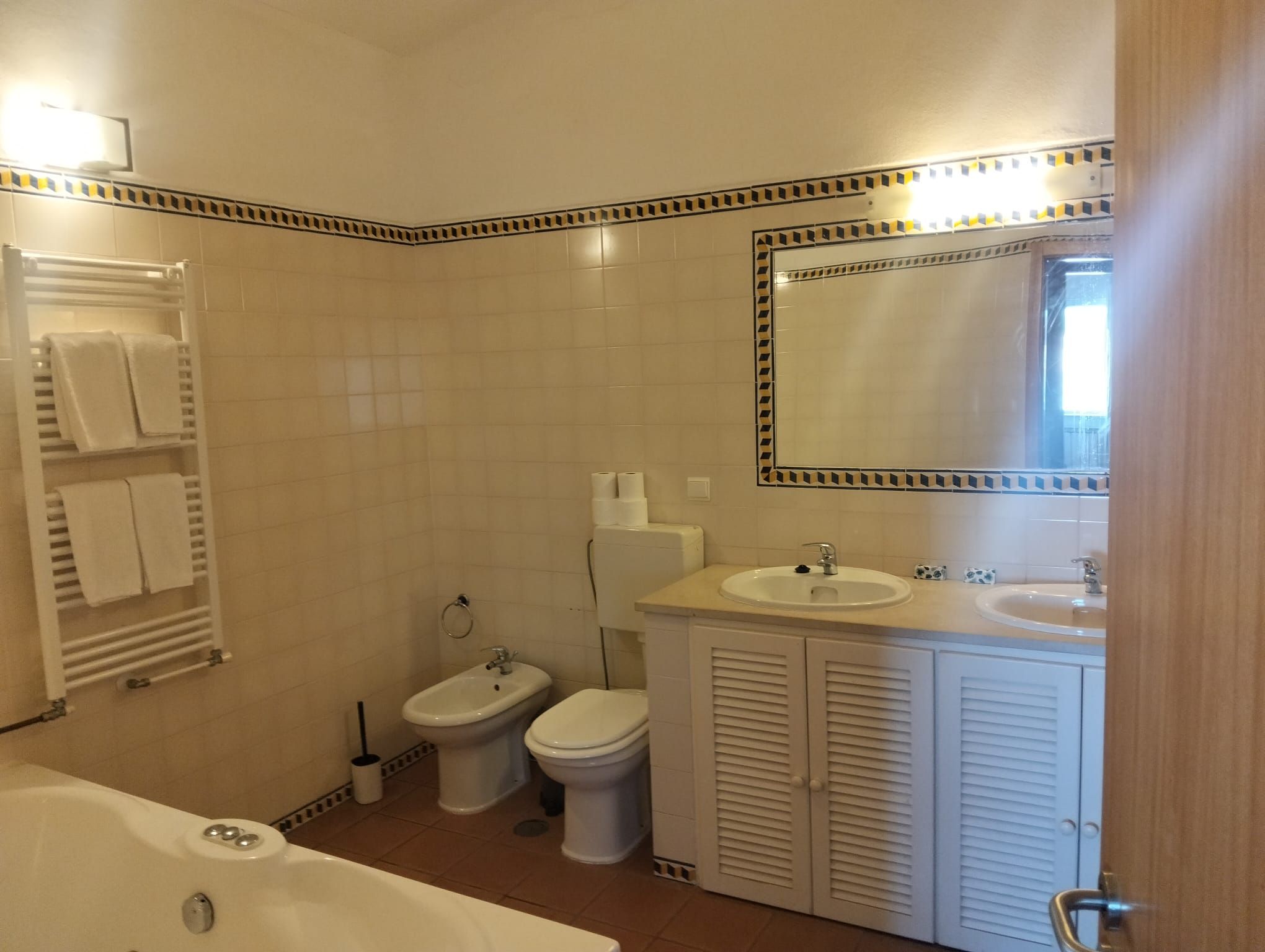 A bathroom with a bathtub, two toilets, a sink, and a mirror.