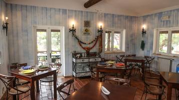 A dining area with wooden tables and chairs, a kitchen in the background, and a decorative garland on the wall.