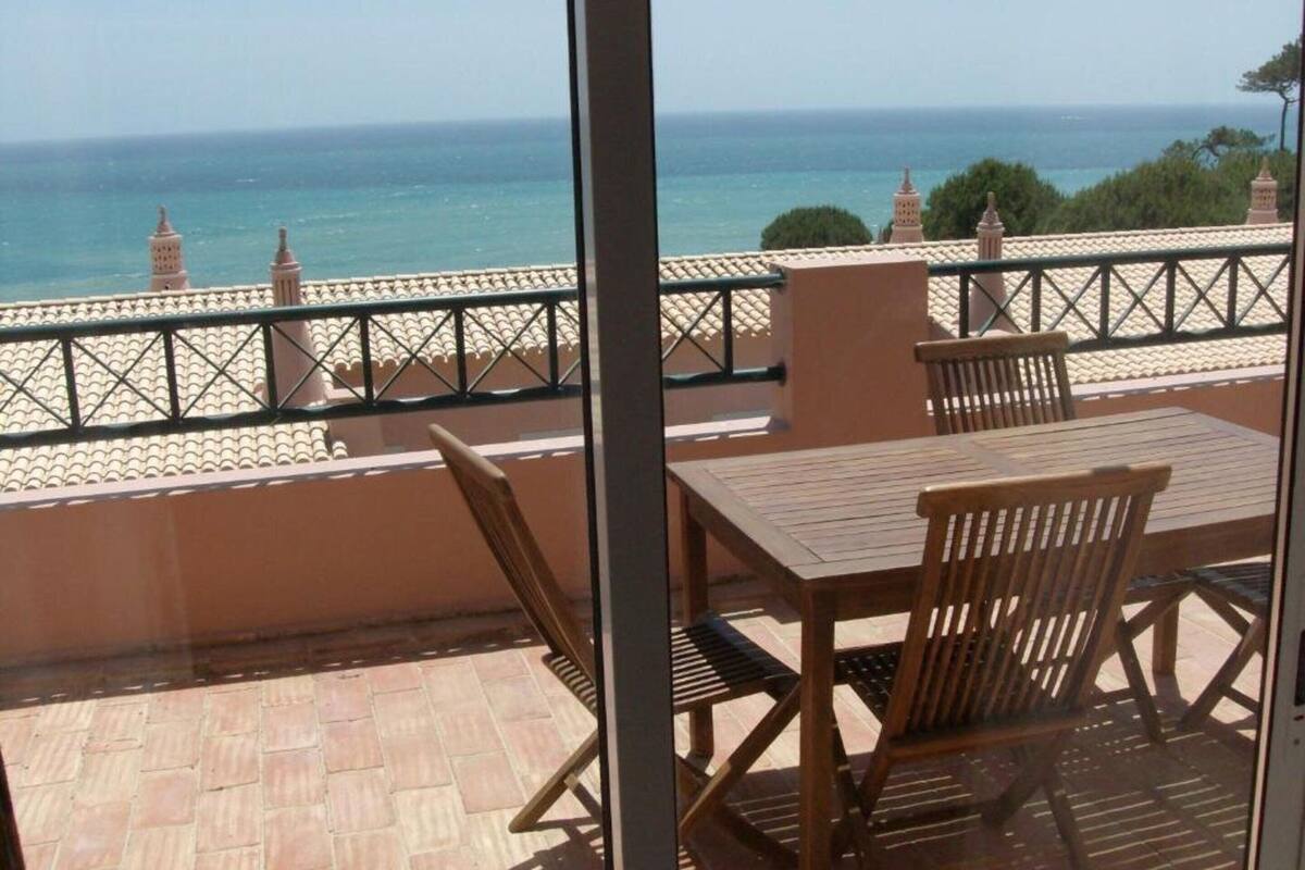 A balcony with a view of the sea, a table, and chairs.
